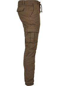 Pantalon cargo marron avec plusieurs poches, taille à cordon de serrage et poignets élastiques, vu de profil.