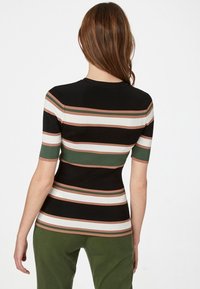 Lyhythihainen toppi, jossa on musta, raidallinen vartalo ja vaaka-kuvioita vihreässä, valkoisessa ja ruosteenpunaisessa värissä. Ribbittexu ja istuva muotoilu.