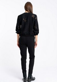 Czarny sweter z teksturowanym wzorem kwiatowym, z luźnymi rękawami i elastycznym dołem, w zestawie z czarnymi slim fit spodniami i botkami za kostkę.