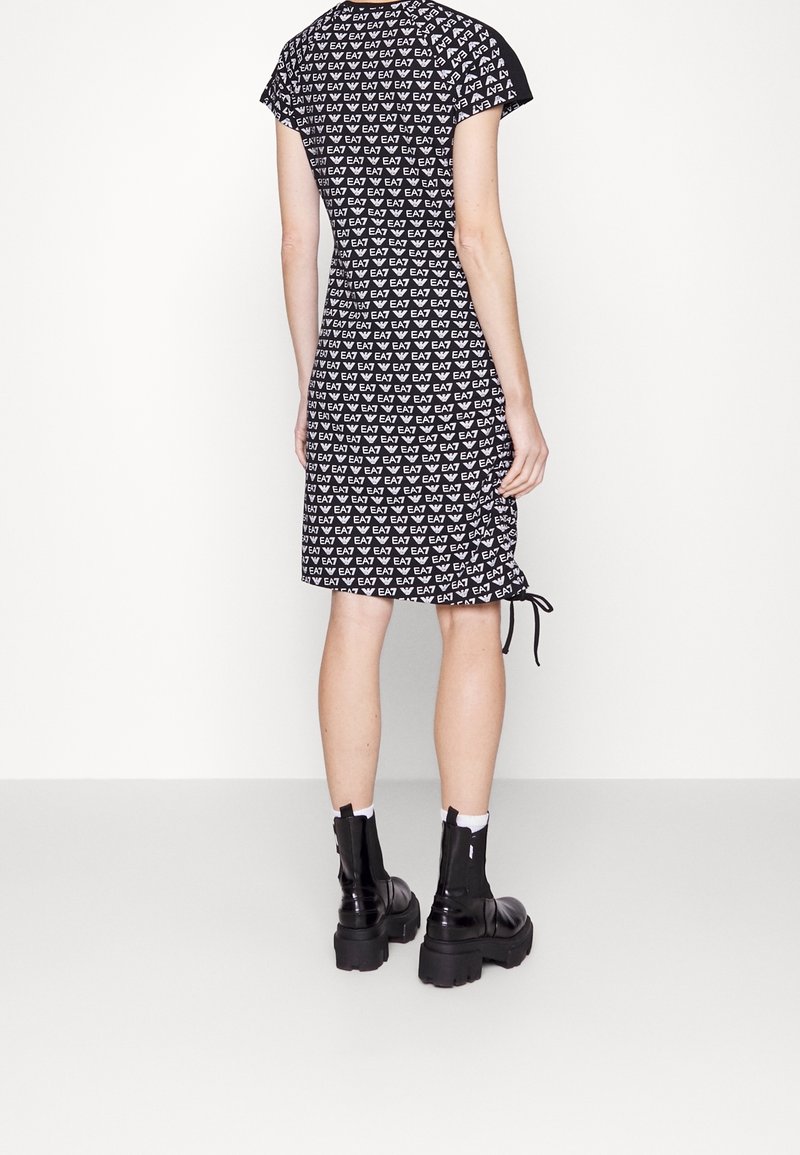Svart och vit kortärmad klänning med ett upprepat logomönster, dragsko-detalj i midjan och kontrasterande svarta ärmar. Åts tillsammans med chunky svarta stövlar.