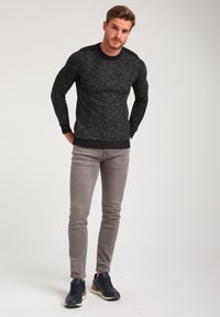 Black textured sweater with a round neckline, paired with slim-fit light gray jeans and navy sneakers. Visual focus on fabric and fit.