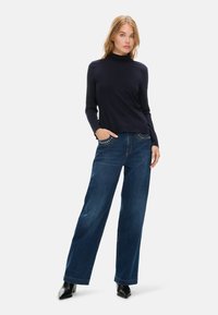 Marineblaues Langarmshirt kombiniert mit weit geschnittenen blauen Jeans mit verzierten Fronttaschen, abgerundet mit schwarzen High Heels.