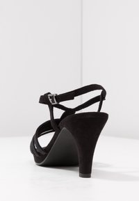 Czarne zamszowe sandały na wysokim obcasie z paskiem wokół kostki, z krzyżującymi się paskami i zwężającym się obcasem. Teksturalny materiał o lekkim połysku.