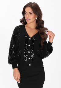 Czarny kardigan z dekoltem w serek, ozdobiony cekinami w diamentowy wzór, z dużymi metalowymi guzikami i bufiastymi rękawami.
