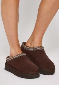Zoccoli in suede marrone con bordi cuciti e decorazioni multicolori. Suola in gomma piatta, design senza retro e punta arrotondata.