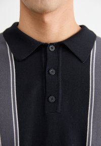 Schwarz- und grau gestreiftes Poloshirt mit einem einfarbigen schwarzen Kragen und vier Knöpfen. Verfügt über einen strukturierten Strickstoff und kontrastierende helle Streifen.