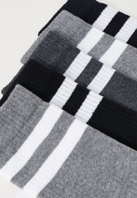 Quatre paires de chaussettes dans des nuances variées de gris, noir et blanc, avec des motifs rayés et des poignets côtelés. Tissu texturé.