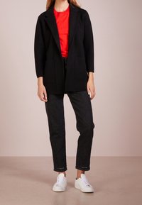 Svart, långärmad kavaj med snedskriven krage och två framfickor, kombinerad med en röd t-shirt och mörka jeans, kompletterad med vita sneakers.