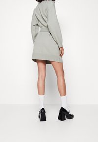 Abito grigio a maglia con vita segnato da una cintura, polsini e orlo a coste. Abbinato a scarpe nere con tacco spesso e calze bianche.