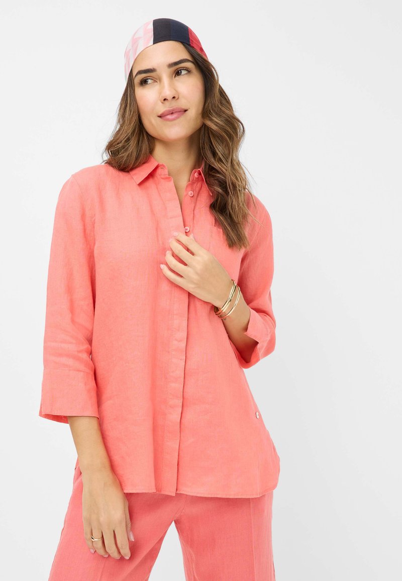 Coral linen shirt with a collar and button-down front, featuring three-quarter sleeves and a relaxed fit. Smooth texture with subtle sheen.