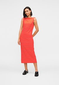 Midi φόρεμα χωρίς μανίκια με κόκκινες και λευκές ρίγες, στενή γραμμή και λαιμόκοψη καραβοσκοινί, συνδυασμένο με μαύρα loafers.