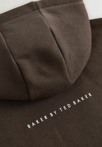Brun hættetrøje med blødt, tekstureret stof; detaljer inkluderer en hætte og en hvid logo "BAKER BY TED BAKER" på ryggen.
