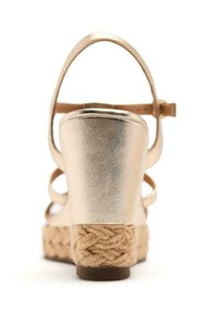 Sandales à talon wedge métalliques dorées avec une plateforme en jute de style espadrille et une sangle à la cheville. Texture lisse avec un motif tressé sur la semelle.