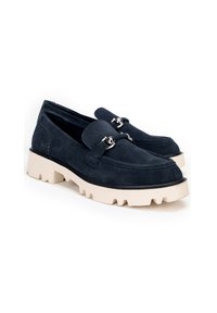 Mocasines de ante azul marino con una suela de goma crema gruesa, que presentan un detalle decorativo de hebilla plateada en el empeine y acentos cosidos.