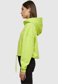 Hoodie cropped di un vivace verde neon, con un grande cappuccio, cordino e maniche lunghe con polsini a costine. Tessuto morbido e texture.