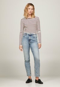 Top a maniche lunghe a righe in bianco e bordeaux, abbinato a jeans a vita alta azzurri chiari. Scarpe nere senza lacci. Design semplice e aderente.