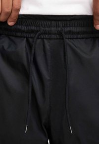 Μαύρα μαγιό σορτς με ελαστική μέση, κορδόνι για κλείσιμο και ομαλή υφή. Διαθέτει αντίθετη μαύρη επένδυση από δίχτυ.