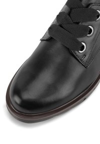 Sneakers din piele neagră cu vârf rotund, șireturi textile și ochiuri metalice. Prezintă un material texturat și o talpă din cauciuc cu un contur brun contrastant.