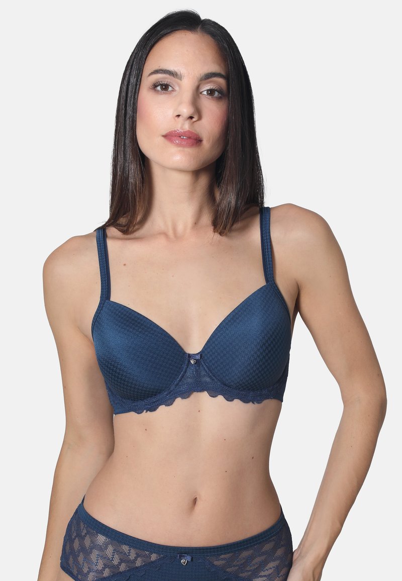 Marineblauer BH mit glatt strukturierten Körbchen, gezackten Rändern und dünnen verstellbaren Trägern. Verziert mit einer dekorativen Schleife in der Mitte.