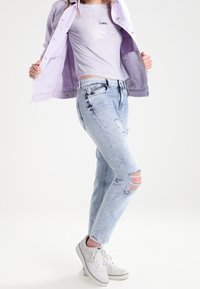 Chaqueta lila sobre una camiseta gris con el texto "Lover", combinada con jeans cortos de mezclilla azul claro y zapatillas blancas.