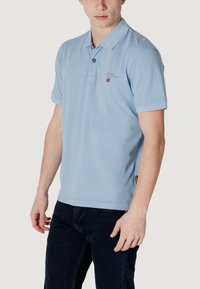 Polo shirt a maniche corte azzurro chiaro con colletto, caratterizzato da un patta con bottoni e un piccolo logo sul petto. Materiale in cotone, vestibilità casual.