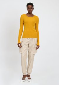 Maglione a maniche lunghe giallo a costine abbinato a pantaloni cargo beige con tasche laterali e polsini elasticizzati. Silhouette semplice, texture morbida.