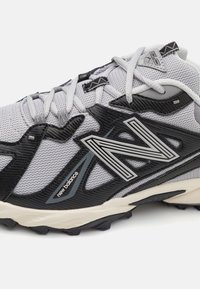 Grijze en zwarte sportschoen met een mesh bovenkant, textuuraccenten, een prominent 'N' logo en een robuuste buitenzool voor grip.