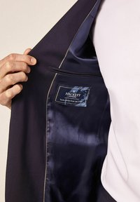 Mornarska sako jakna s glatkom satenskom podstavom. Unutrašnjost ima oznaku logotipa, kontrastne šavove i unutarnji džep.