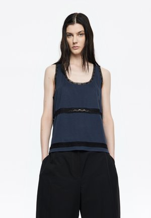 Camiseta de tirantes de color azul marino con detalles de encaje alrededor del escote y el dobladillo, que presenta rayas horizontales de encaje. Fabricada con tejido suave, tiene un corte holgado.