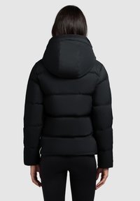 Sort pufferjakke med en stor hætte, quiltet design og en tætsiddende silhuet. Har elastiske manchetter og sidelommer. Glat tekstur.