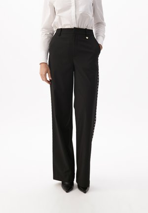 Black pinstriped trousers with a straight leg, featuring side buttons and a smooth texture. Paired with a white button-up shirt and black heels.