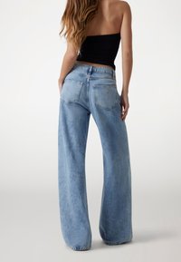Jeans de tiro alto en denim de color azul claro y de pierna ancha, con bolsillos traseros y una etiqueta de logo cerca de la cinturilla. Textura suave.