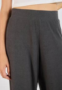 Pantalon gris côtelé avec une large ceinture et des rayures verticales, fabriqué dans un tissu doux présentant une texture subtile et un tombé fluide.