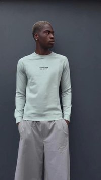 Sweat-shirt vert menthe clair avec un col rond, des manches longues et un logo imprimé. Assorti à un pantalon plissé léger gris clair, ample.