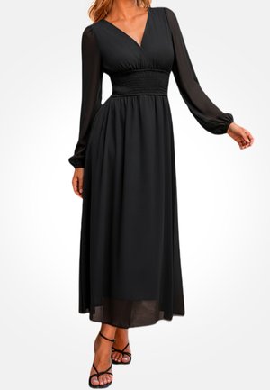 Schwarzes langärmliges Kleid mit V-Ausschnitt und geraffter Taille. Leichter, fließender Stoff mit transparentem Überzug und knöchellangem Saum. Riemchensandalen.