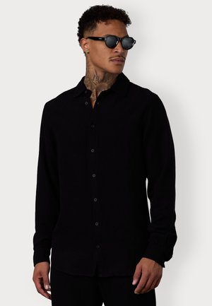 Black long-sleeve button-up shirt with a collared neckline and a relaxed fit. Features a smooth texture and black buttons along the front.