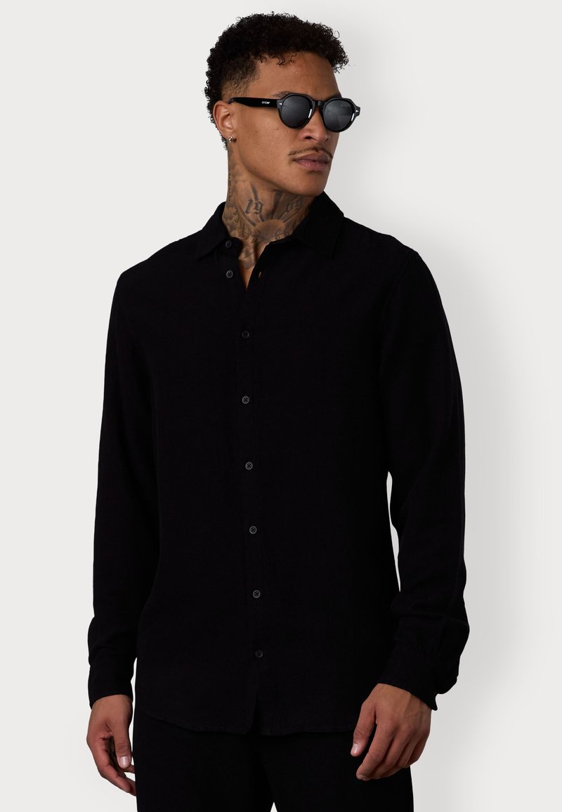 Schwarzes Langarmhemd mit Knopfleiste, klassischem Kragen und lockerer Passform. Mit glatter Textur und schwarzen Knöpfen auf der Vorderseite.