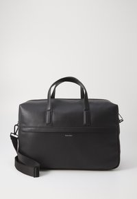 Sac de voyage en cuir noir avec une surface texturée, des poignées doubles, une bandoulière réglable et un logo de marque subtil à l'avant.