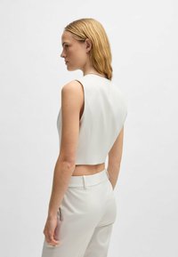 Weißes kurz geschnittenes Top mit ärmellosem Design und klaren Linien, ausgestattet mit einer glatten Textur und minimalistischem Stil, kombiniert mit passender Hose.