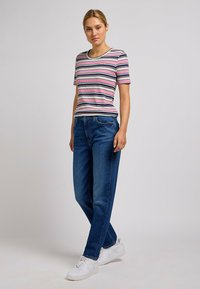 Pasiasty, prążkowany t-shirt w kolorach różowym, białym i zielonym, z okrągłym dekoltem; w komplecie z prostymi, niebieskimi dżinsami i białymi trampkami.