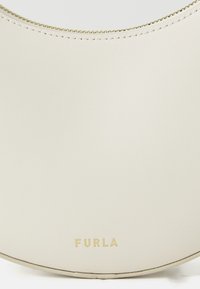 Round cream-colored leather handbag with a smooth texture, gold hardware, and embossed brand name 'FURLA' at the bottom.