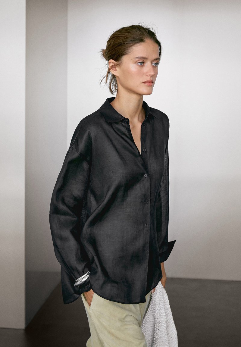 Camicia nera con bottoni, colletto, realizzata in un tessuto leggero e leggermente texturizzato. Vestibilità comoda con maniche lunghe e design minimale.
