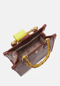 Sac à main en simili-cuir crocodile marron avec poignées en bambou, accent en cuir jaune, et un intérieur spacieux avec doublure claire et motif de logo.