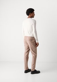 Chemise blanche à manches longues au design ajusté, associée à un pantalon en lin marron clair avec taille à cordon, vue de dos.