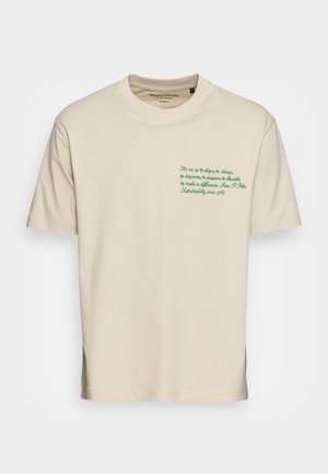 T-shirt en coton beige avec des manches courtes, un col rond et un texte brodé vert en haut à gauche de la poitrine.