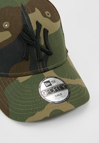 Camouflage cap in green and brown cotton material, featuring an embroidered black logo and a round adjustable size tag.