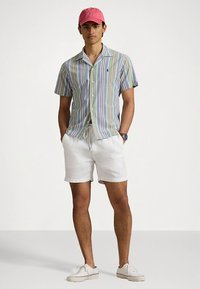 Πουκάμισο με κοντά μανίκια και κατακόρυφες πολύχρωμες ρίγες, συνδυασμένο με λευκά σορτς και ροζ καπέλο. Ελαφρύ ύφασμα και άνετη εφαρμογή.