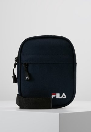 Lille navyblå FILA crossbody taske med frontlynlåslomme og justerbar sort rem på hvid overflade.