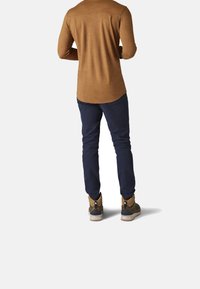 Felpa marrone a maniche lunghe con un orlo curvo, abbinata a pantaloni blu navy. Le scarpe presentano un design beige e grigio con una cavigliera alta.