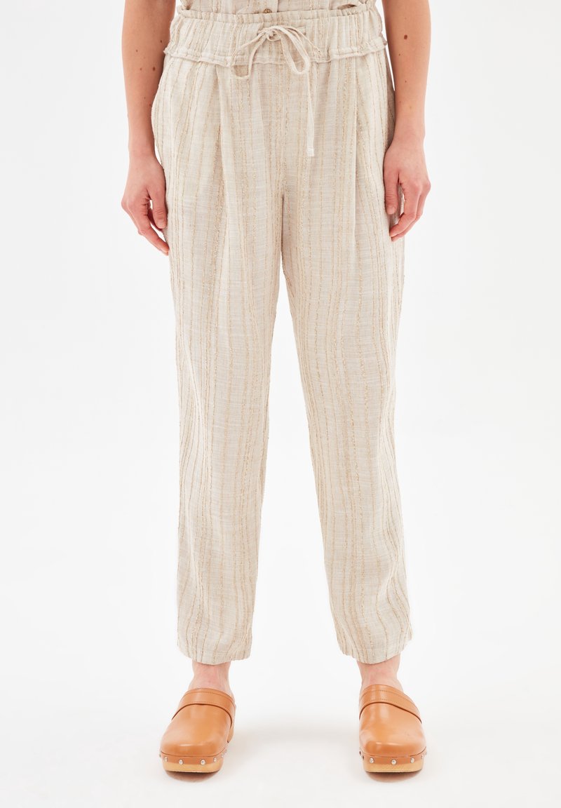Pantalon beige texturé à cordon porté avec des sabots en cuir marron clair avec des clous métalliques sur les bords des semelles.